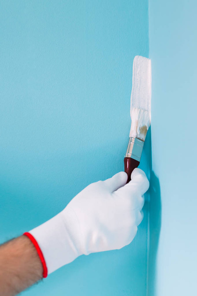 Image of man holding paintbrush and painting blue wall. - 写真・画像