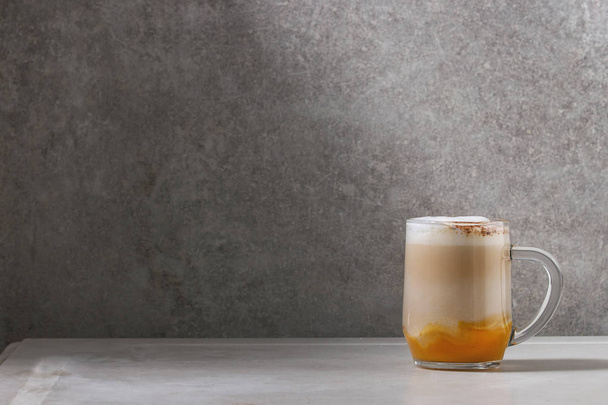 Glass of pumpkin layered spice latte with pumpkin puree, milk foam and cinnamon standing on white marble table with grey wall at background. Copy space - Valokuva, kuva