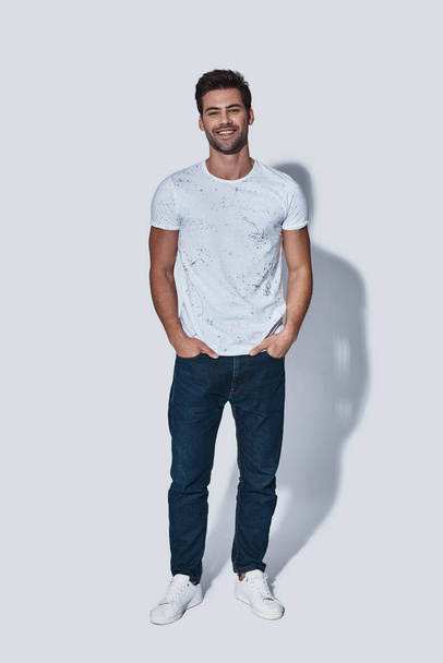 happy handsome man in casual wear looking at camera and smiling while standing against grey background - Fotoğraf, Görsel