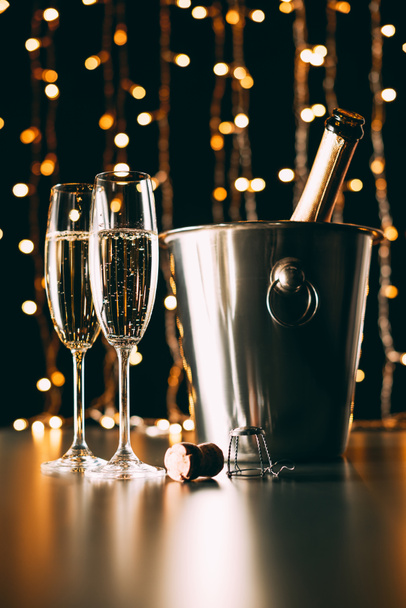 champagne bottle in bucket and glasses on garland light background, christmas concept - Foto, immagini