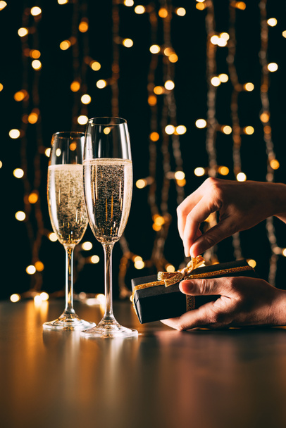 image recadrée de femme ouvrant présent près de verres de champagne sur fond de guirlande, concept de Noël
 - Photo, image