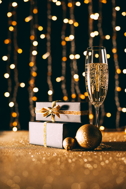 surface level of champagne in glass and gift boxes on garland light background, christmas concept - Foto, afbeelding