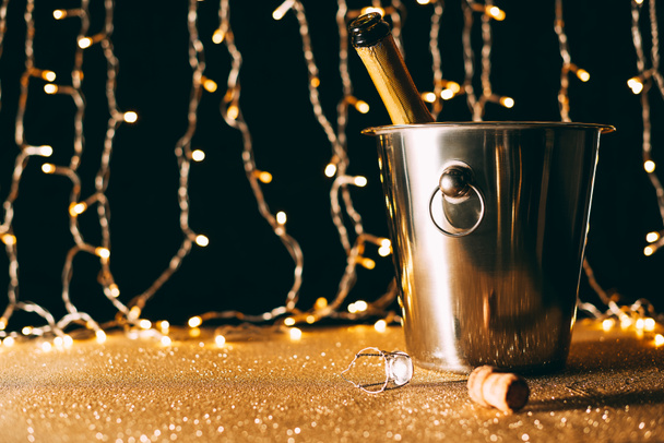 champagne bottle in bucket on garland light background, christmas concept - Фото, зображення