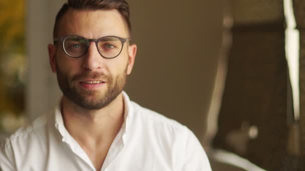 Handsome businessman in glasses looking at camera. A man in a white shirt smiles, puts on his glasses. Lucky businessman, office employee, financier - Materiał filmowy, wideo