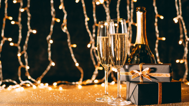 twee glazen van champagne, presenteert en fles op garland licht achtergrond, Kerstmis concept - Foto, afbeelding