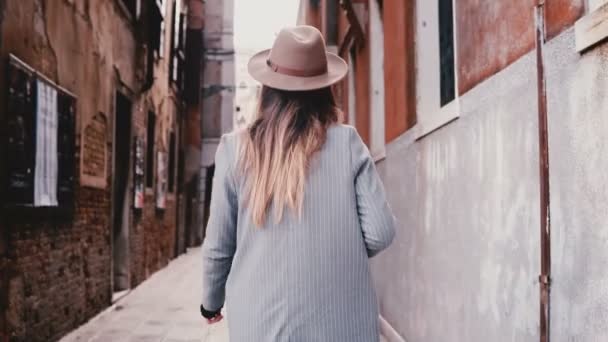 Back view of professional travel blogger girl with camera enjoying exploring ancient narrow streets in Venice, Italy. - Video