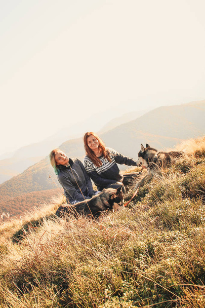 Two girl in the top of mount play with  two husky. Ukrainian Carpathians in autumn time. Warm colored green leaves.Forests and mountains view. Travel with dog - Фото, зображення