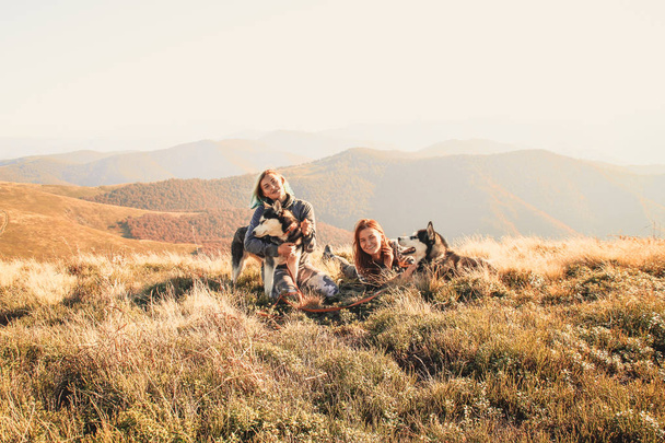 zwei Mädchen in der Spitze des Berges spielen mit zwei Huskys. Ukrainische Karpaten im Herbst. warm gefärbte grüne Blätter. Blick auf Wälder und Berge. Reise mit Hund - Foto, Bild