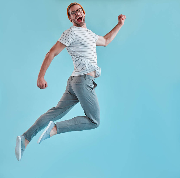 Handsome man isolated. Stylish young man in eyeglasses is jumping and posing on blue background. - Fotoğraf, Görsel