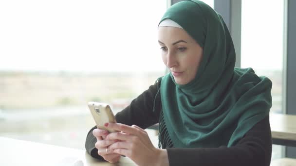 Portrait pretty muslim woman in hijab sitting at the table and uses the phone,slow mo - Video