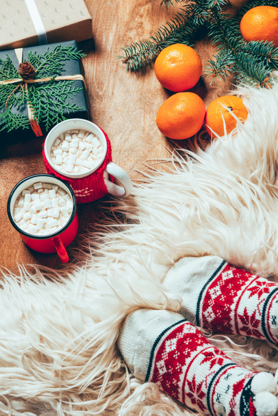 partial view of woman in socks on background with cups of cocoa drink, tangerines, cookies and christmas presents - Photo, Image
