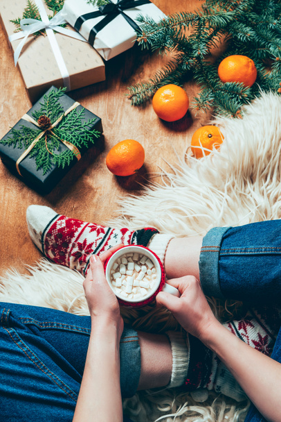 részleges kilátás nő csésze forró csokoládé és fehérmályva háttérrel, karácsonyi ajándékok és mandarin  - Fotó, kép
