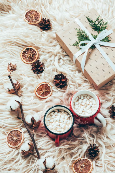 flat lay with cup of cocoa with marshmallows, wrapped christmas present and cotton twig on woolen background - Zdjęcie, obraz