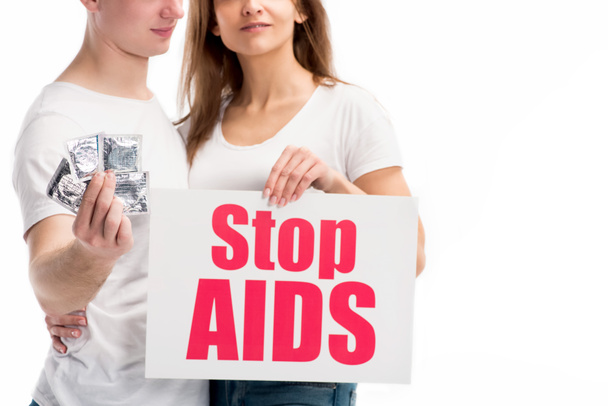 περικομμένη εικόνα του φίλο κρατώντας προφυλακτικά και φίλη παρουσίαση της κάρτας με stop aids κείμενο απομονωθεί σε λευκό - Φωτογραφία, εικόνα