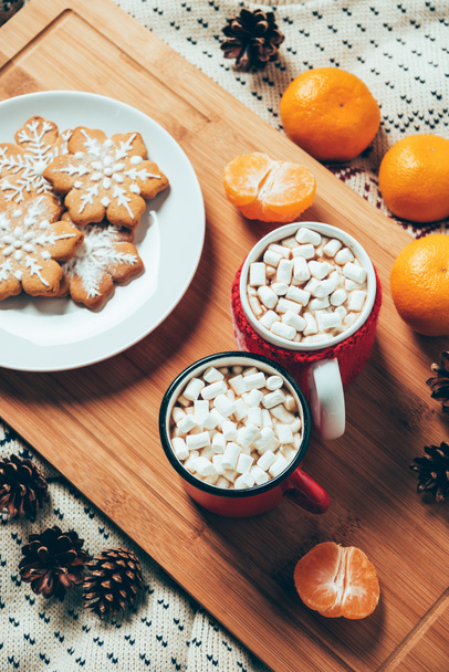 top view of cups of hot chocolate with marshmallows, cookies and tangerines on blanket background, christmas breakfast concept  - Photo, Image