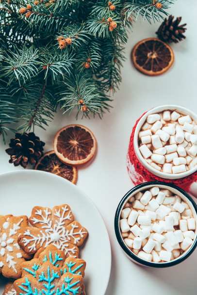 top view of cups of hot chocolate with marshmallows, cookies and pine tree branches on white surface, christmas breakfast concept - Zdjęcie, obraz
