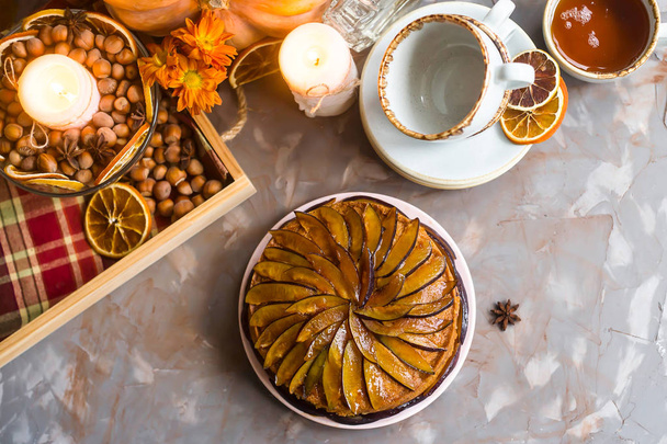 Plum cake decorated with sliced plum among the autumn decor - pumpkin, candle, oranges and yellow chrysanthemum. Rustic style. Homely cozy flat lay. Top view - Photo, Image