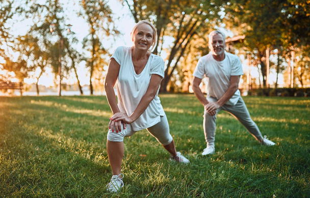 Senior couple is doing sport outdoors. Stretching in park during sunrise. Doing yoga together. Healthy lifestyle concept - Foto, immagini