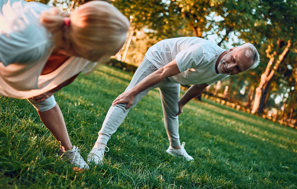 Senior paar doet sport buitenshuis. Die zich uitstrekt in park tijdens zonsopgang. Yoga samen te doen. Gezonde levensstijl concept - Foto, afbeelding