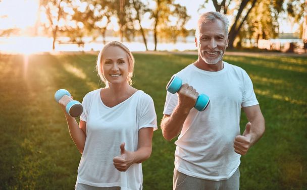 Senior couple is doing sport outdoors. Stretching in park during sunrise. Doing yoga together. Healthy lifestyle concept - Фото, зображення