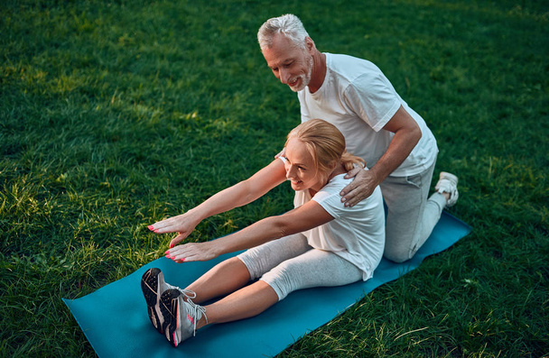 Senior couple is doing sport outdoors. Stretching in park during sunrise. Doing yoga together. Healthy lifestyle concept - Photo, image