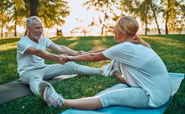 Senior couple is doing sport outdoors. Stretching in park during sunrise. Doing yoga together. Healthy lifestyle concept - Zdjęcie, obraz