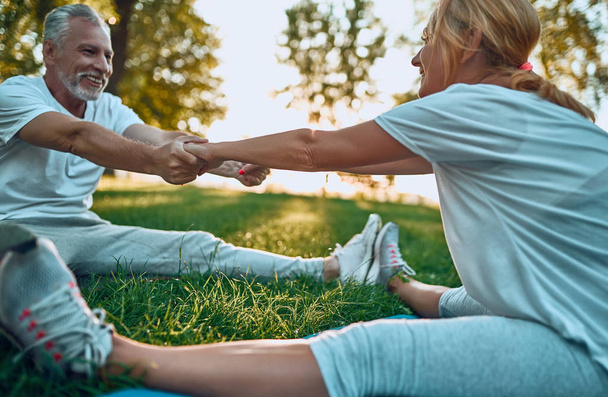 Senior couple is doing sport outdoors. Stretching in park during sunrise. Doing yoga together. Healthy lifestyle concept - Fotó, kép