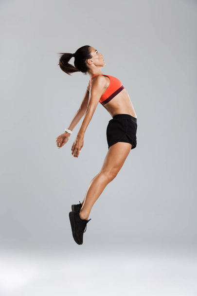 Image of a beautiful strong young sports woman jumping isolated indoors. - Фото, зображення