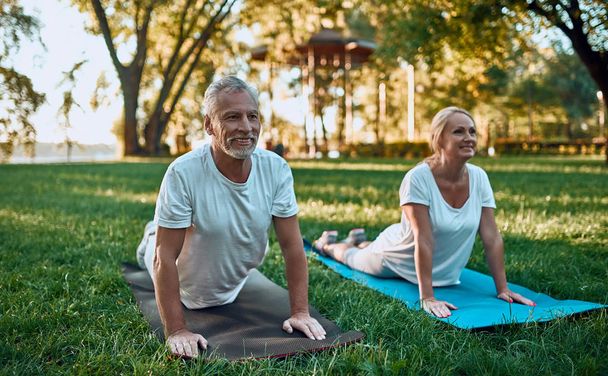 Senior couple is doing sport outdoors. Stretching in park during sunrise. Doing yoga together. Healthy lifestyle concept - Foto, Bild
