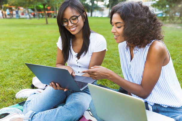 Image of cheerful young girls in park using laptop computers on grass. - Foto, Imagem