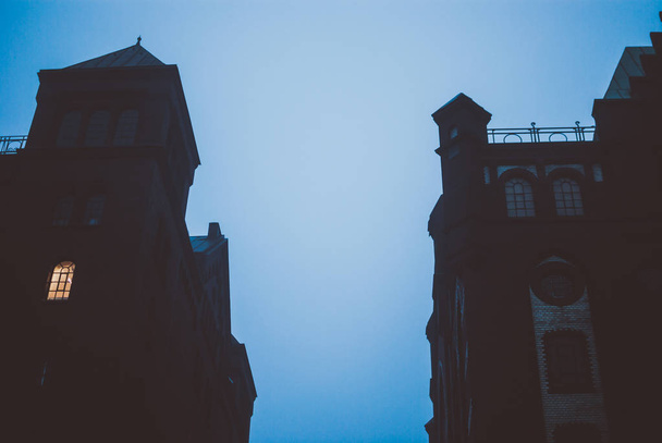 Ciel nocturne bleu foncé entre deux bâtiments sombres et ombragés dans la ville de Hafen à Hambourg, en Allemagne. Brouillard gris épais recouvrant les bâtiments en briques rouges. Vue gothique obscure
. - Photo, image