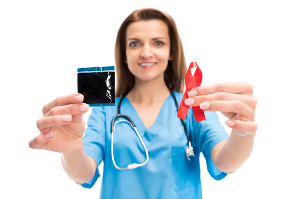 lächelnder attraktiver Arzt mit Kondom und roter Schleife auf weißem, Welt-Aids-Tag-Konzept - Foto, Bild