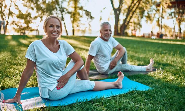 Senior couple is doing sport outdoors. Stretching in park during sunrise. Doing yoga together. Healthy lifestyle concept - 写真・画像
