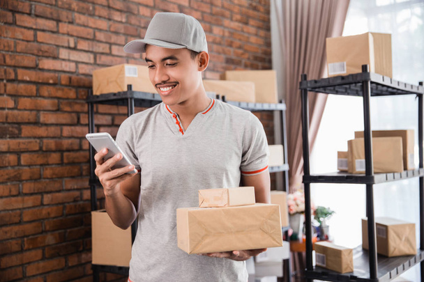 man with package holding smartphone - Foto, imagen