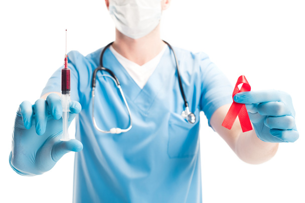 cropped image of doctor in medical mask holding red ribbon and syringe with blood isolated on white, world aids day concept - Photo, Image