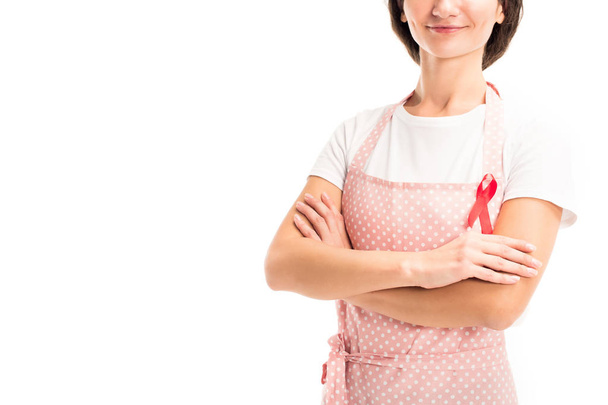 cropped image of housewife in pink apron and red ribbon standing with crossed arms isolated on white, world aids day concept - Фото, зображення