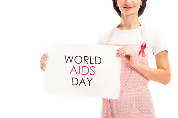 cropped image of housewife in pink apron and red ribbon showing world aids day card isolated on white - Zdjęcie, obraz