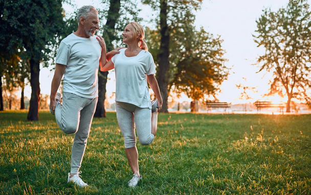 Senior couple is doing sport outdoors. Stretching in park during sunrise. - Foto, Imagem