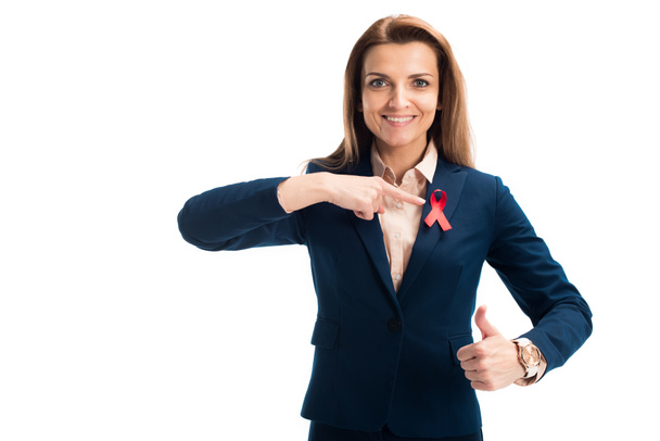 Lächelnde attraktive Geschäftsfrau zeigt auf rotes Band und zeigt Daumen hoch auf weißem, Welthilfetag-Konzept - Foto, Bild