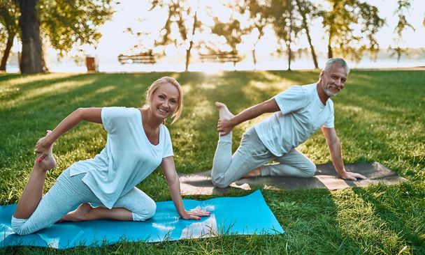 Senior couple is doing sport outdoors. Stretching in park during sunrise. - Fotoğraf, Görsel