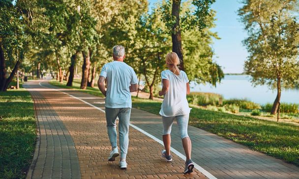 Senior couple is doing sport outdoors. Running in park in the morning. - 写真・画像