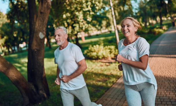 Ανώτερος ζευγάρι κάνει αθλητισμό σε εξωτερικούς χώρους. Τρέξιμο στο πάρκο το πρωί. - Φωτογραφία, εικόνα