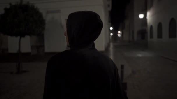 Achterzijde van een gemaskerde jonge man lopen op straat 's nachts - Video