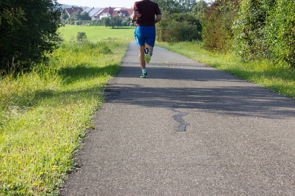 Ejercicio al aire libre corriendo hombre en septiembre temporada de otoño en el sur de Alemania con césped verde al lado y el clima soleado
 - Foto, Imagen