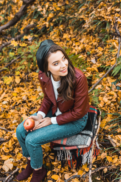 high angle view of fashionable young woman in beret and leather jacket holding apple outdoors  - Fotó, kép