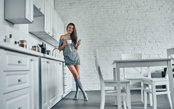 Good morning! Attractive young woman is having rest at home. Full-length image of girl on kitchen. - Foto, afbeelding