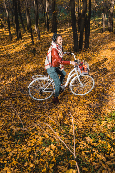 high angle view of girl in leather jacket and beret riding on bicycle in yellow autumnal forest - Zdjęcie, obraz