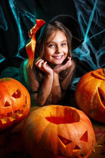 Vrolijke Halloween. Mooi klein kind meisje in heks kostuum met snijwerk pompoen. Voorbereiden van Halloween en gelukkige familie. - Foto, afbeelding