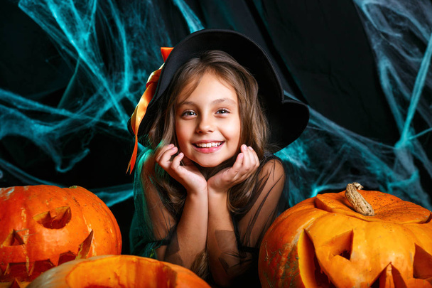Happy halloween. Pretty little child girl in witch costume with carving pumpkin . Happy family preparing for Halloween. - Фото, изображение