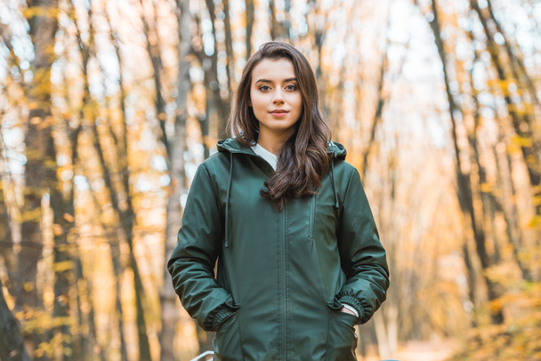 beautiful young woman in jacket looking at camera in autumnal forest - Foto, imagen